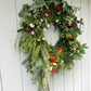 Decorative wreath with greenery, red berries, and white flowers on a wooden door.