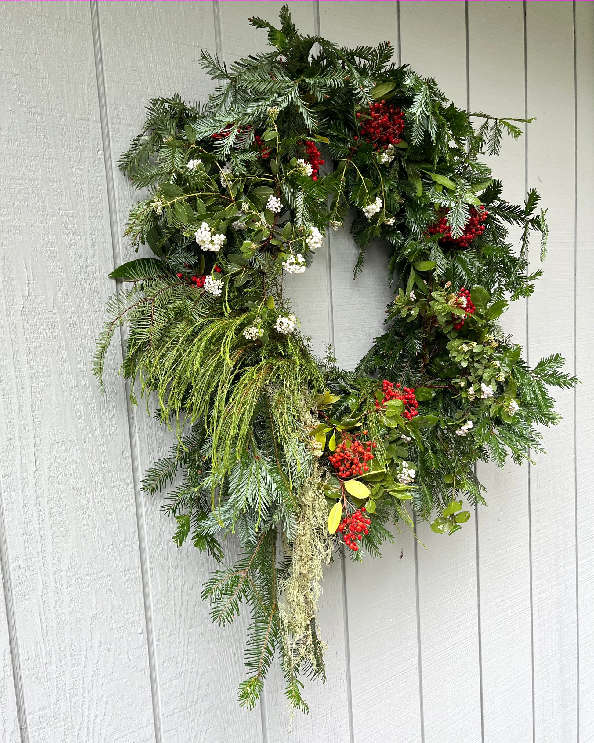 Decorative wreath with greenery, red berries, and white flowers on a wooden door.