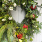 Decorative wreath with greenery, red berries, and white flowers on a white door.