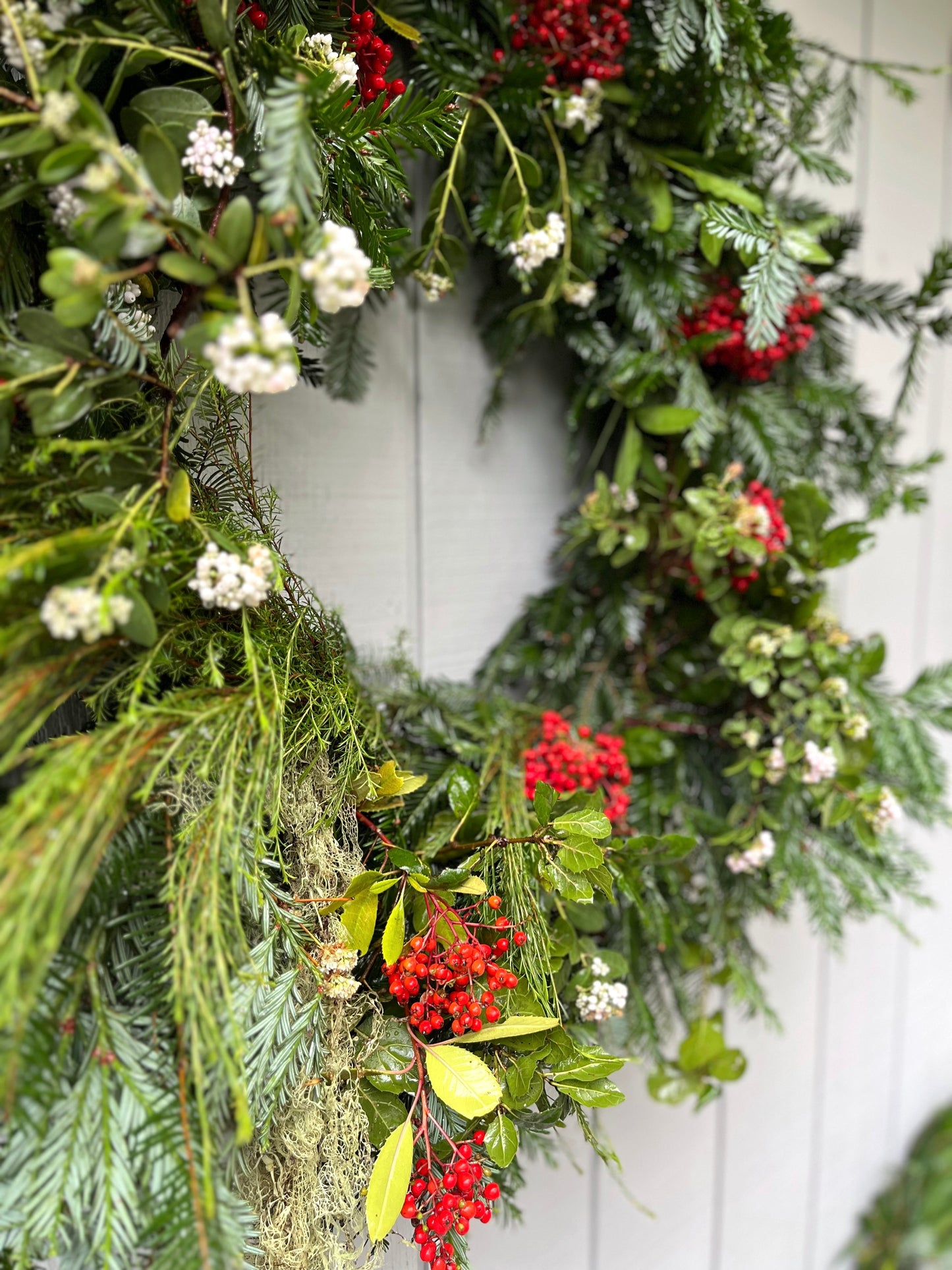Decorative wreath with greenery, red berries, and white flowers on a white door.
