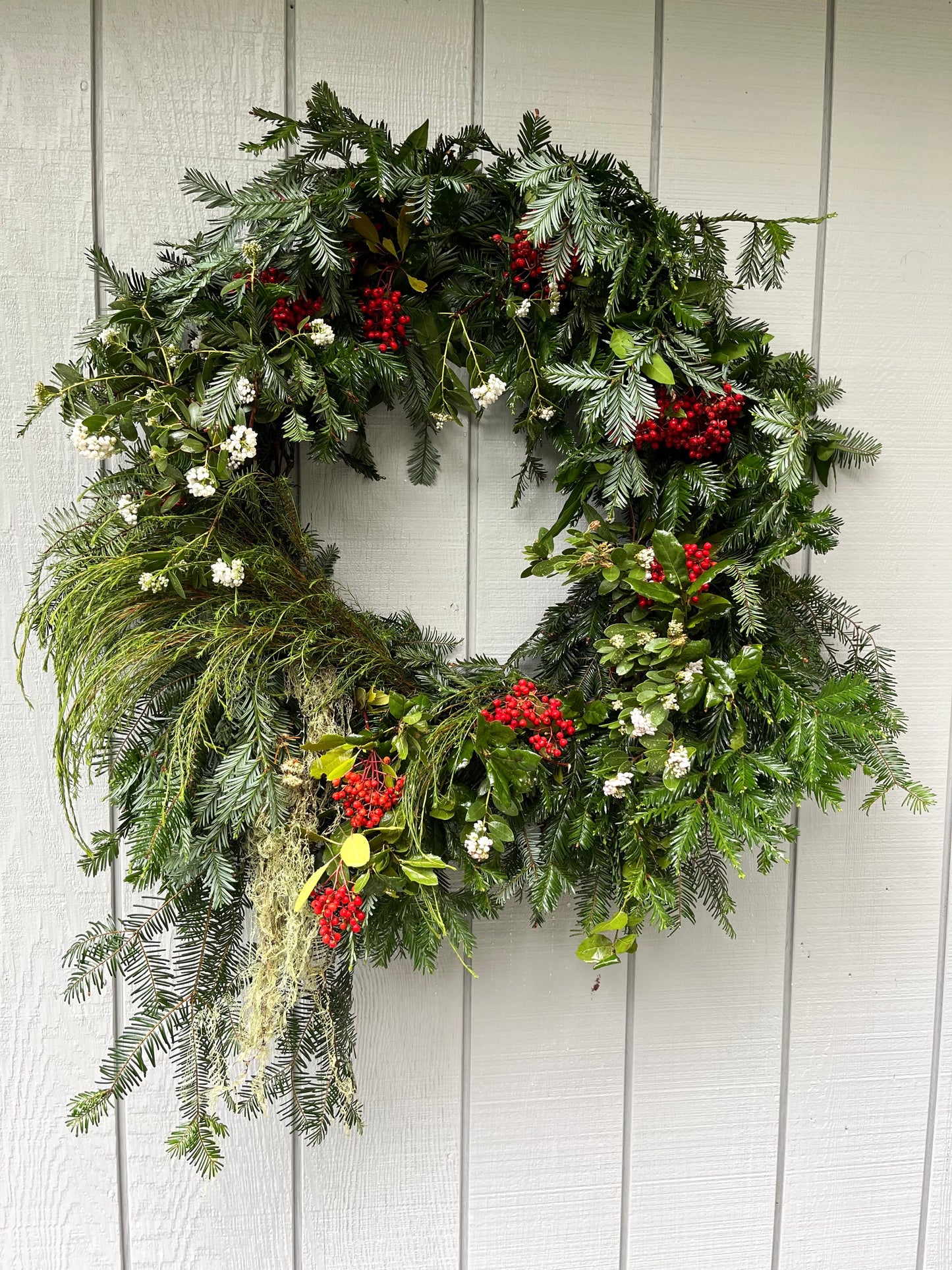 Green wreath with red berries and white flowers on a light wooden background