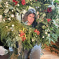 Person holding a large Christmas wreath with greenery and berries indoors.