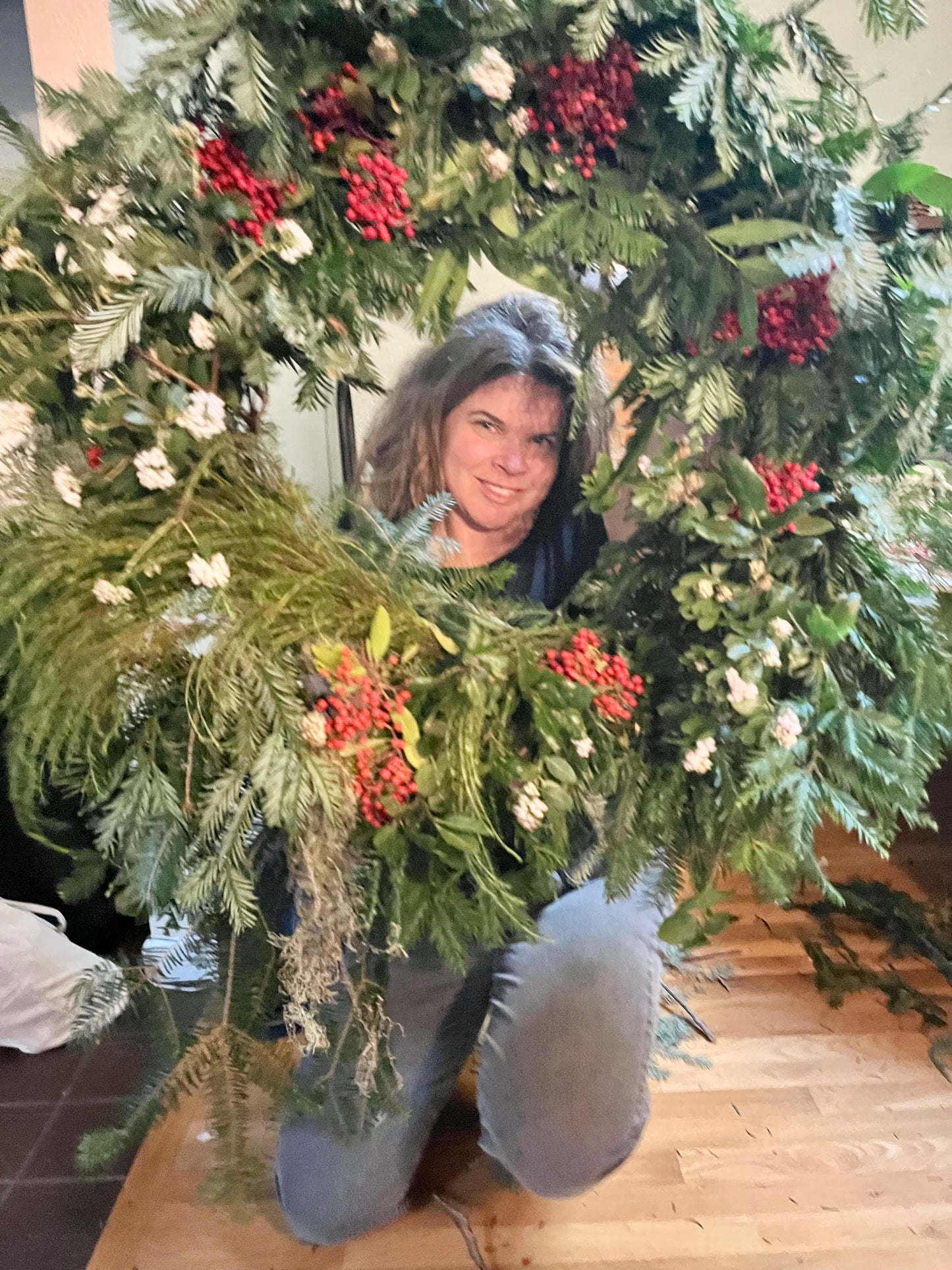 Person holding a large Christmas wreath with greenery and berries indoors.