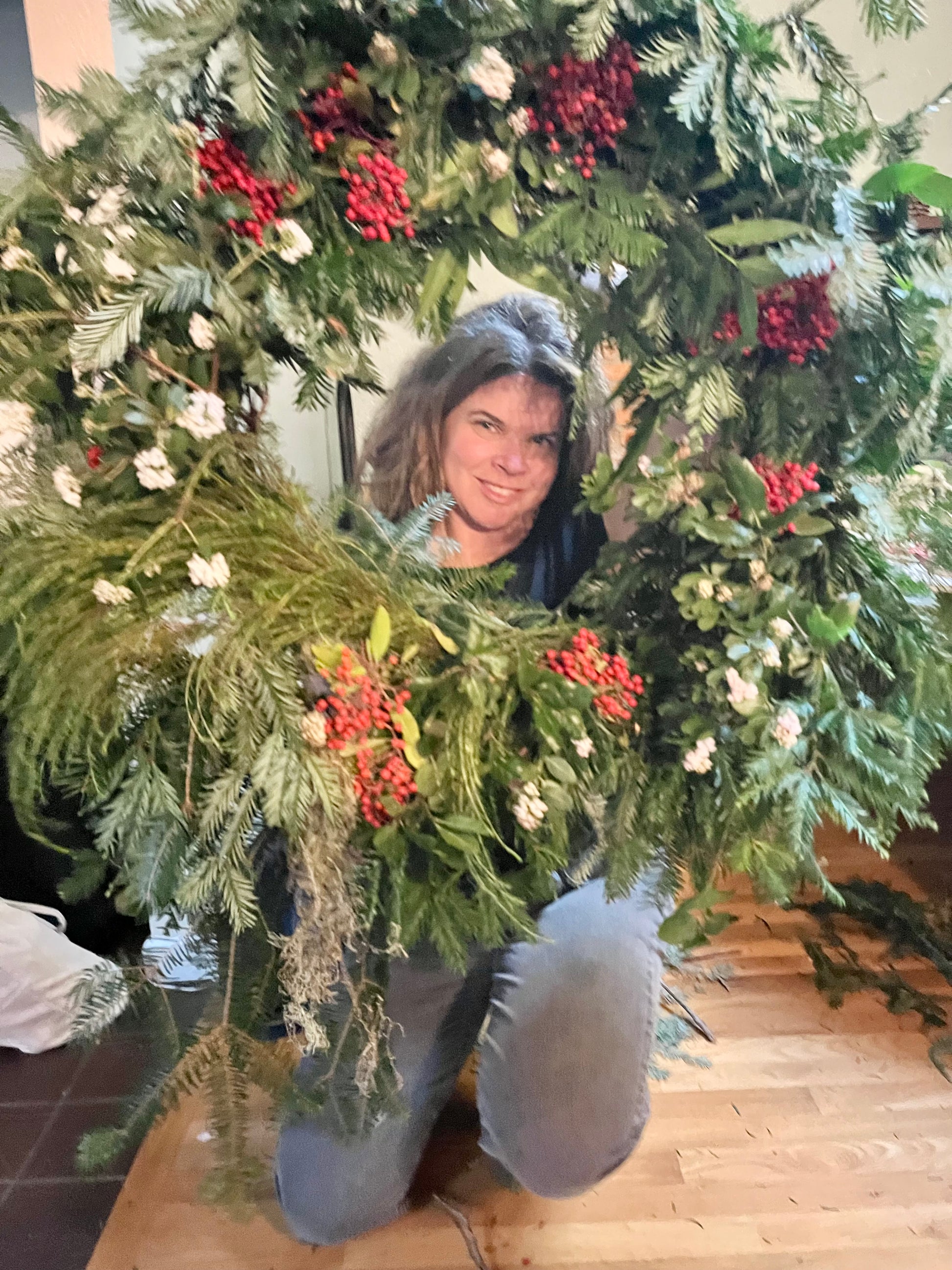 Person holding a large Christmas wreath with greenery and berries indoors.